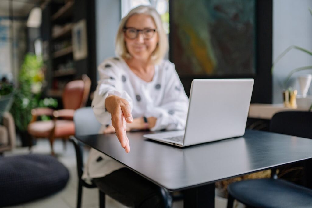 Woman holding out hand (in focus). Out of focus is laptop and office.