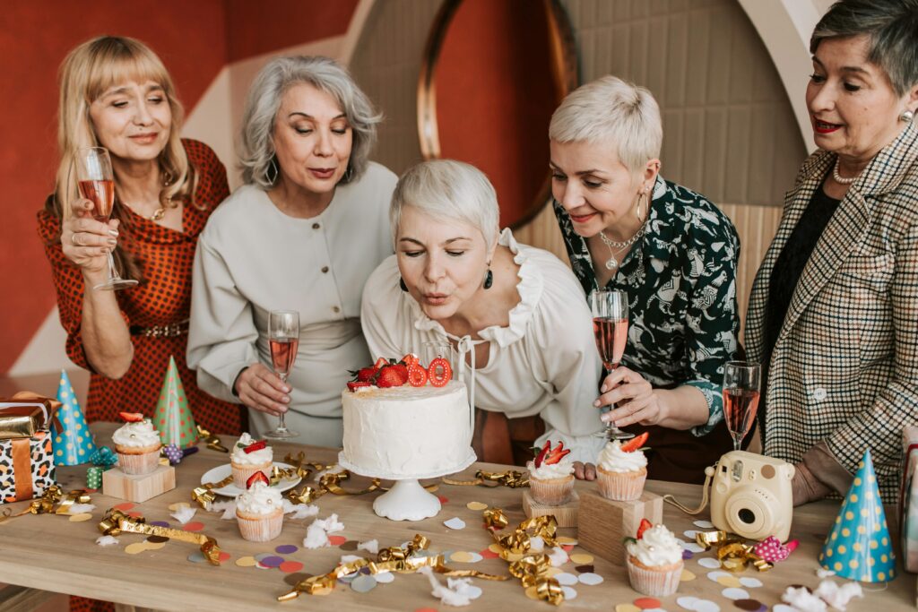 Brain health boost with social connections. A group of senior women celebrating a birthday with cake and drinks indoors.