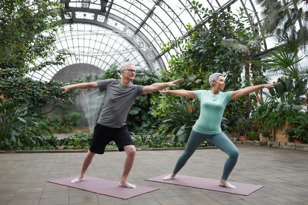 Elderly couple enjoying yoga exercises together in a lush greenhouse setting.